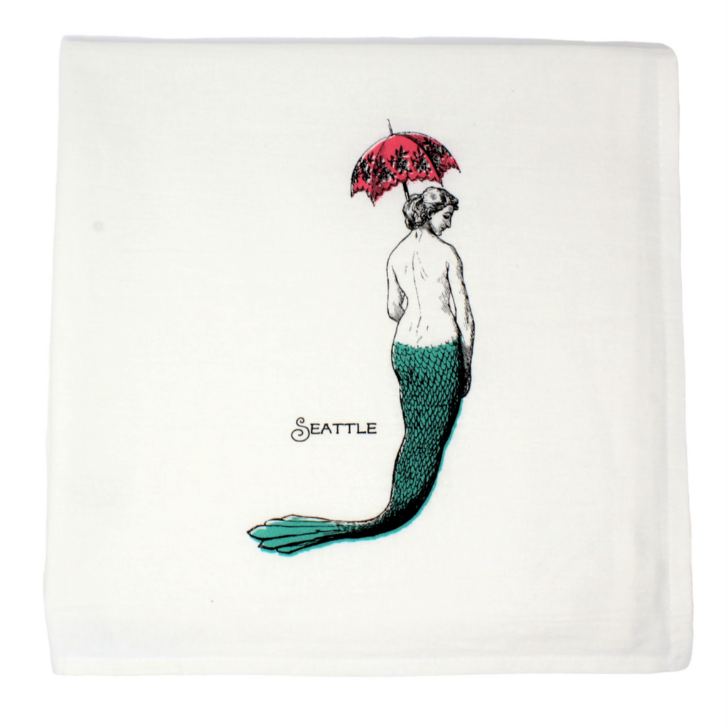 White flour sack towel with vintaged inspired design of mermaid silhouette with a teal tail and pink parasol.  Seattle is written in script. 